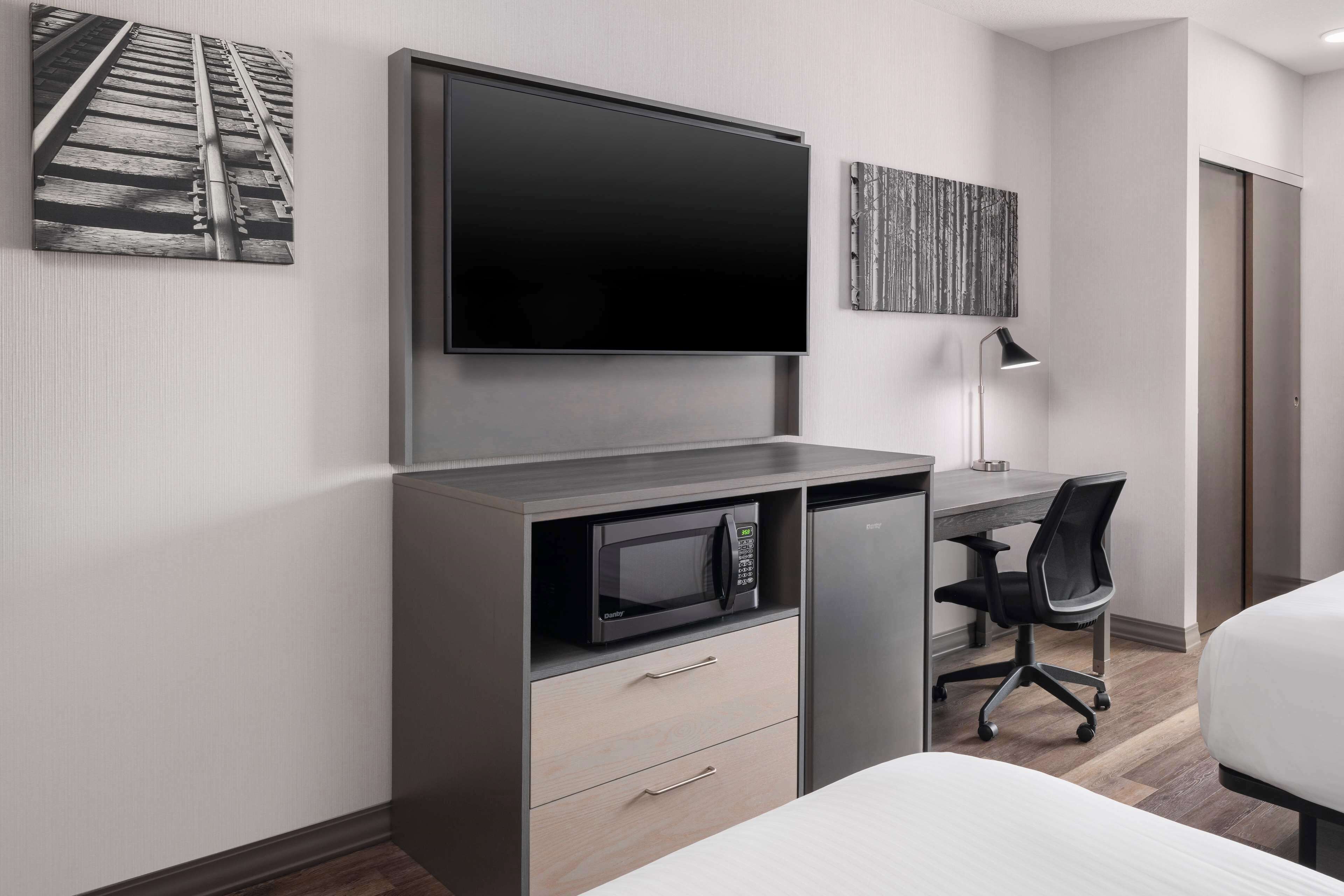 Een hotelkamer met een flatscreen televisie aan de muur, een magnetron, een bureau met stoel en een bed.