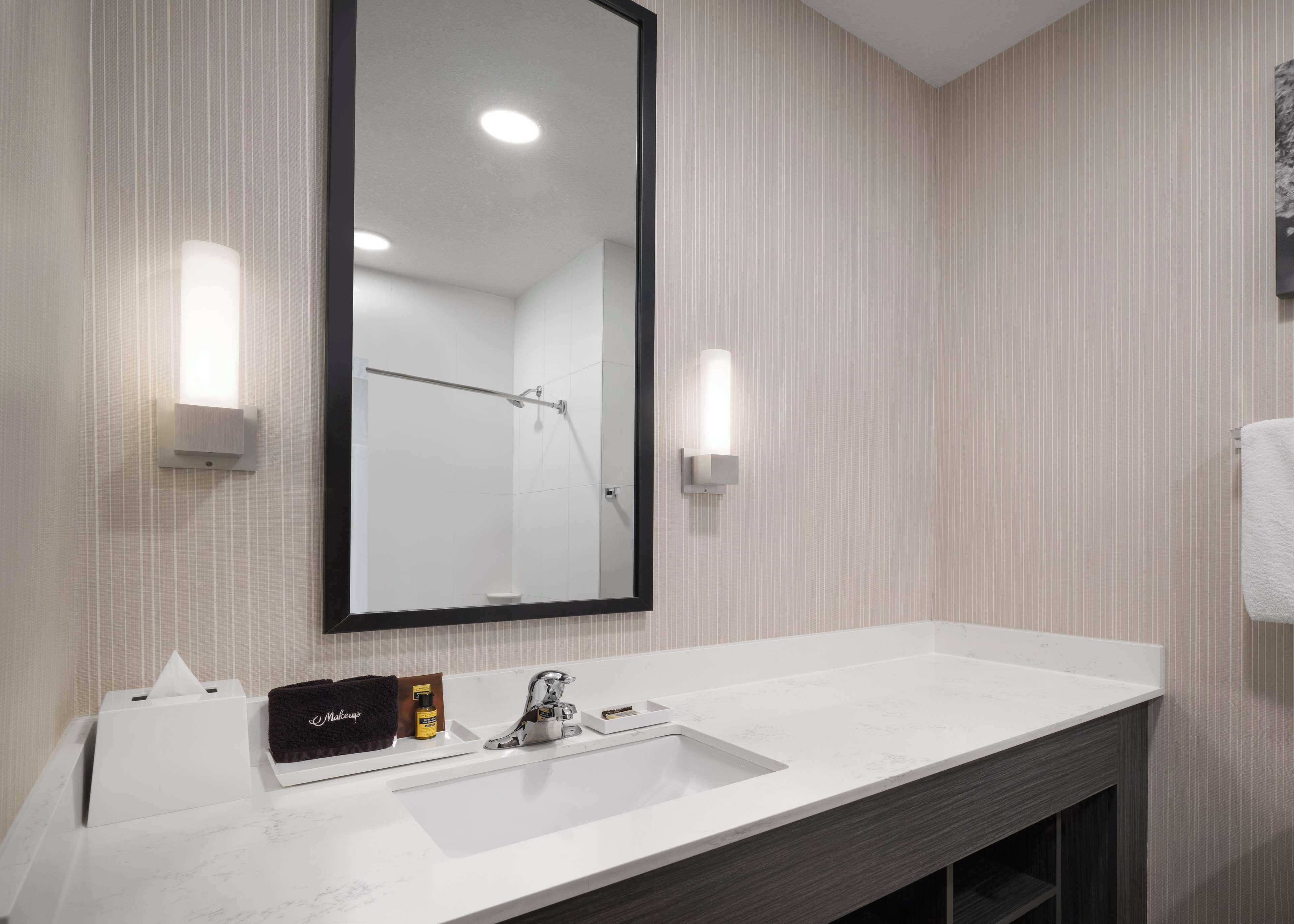 A hotel bathroom with a large mirror, a white sink, and two wall-mounted lights.