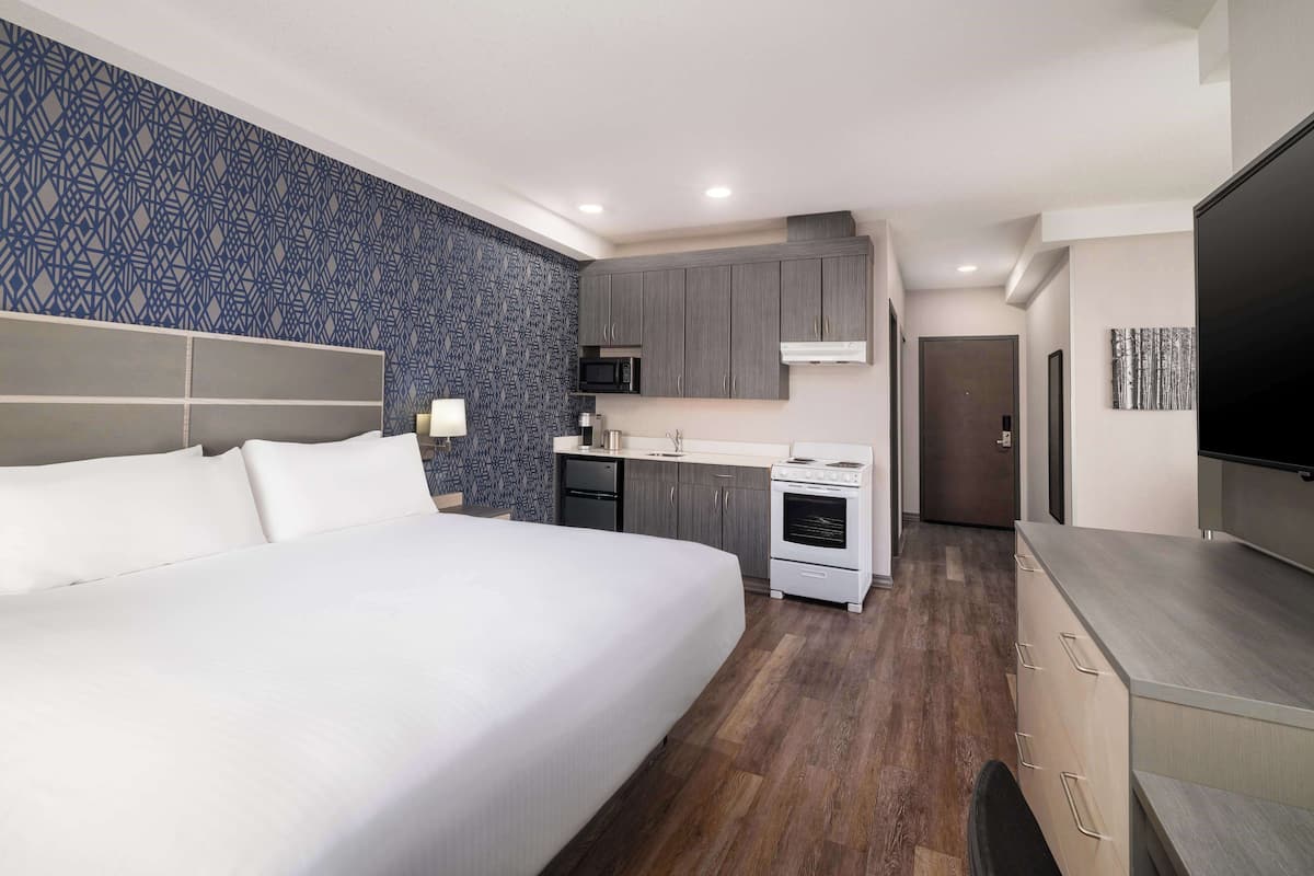 Ein Hotelzimmer mit einem großen Bett, einer Küchenzeile und einem Fernseher.