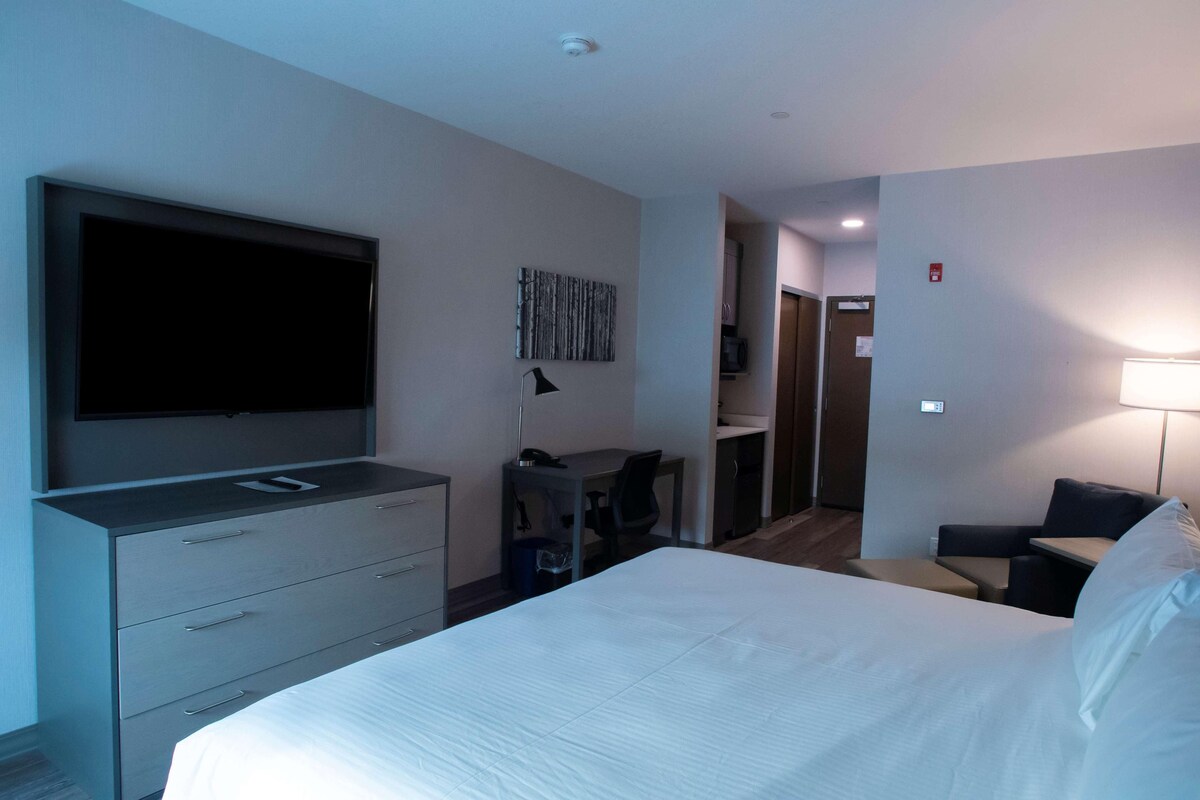 A hotel room with a large bed, a desk with a chair, a flat-screen TV, and a small seating area with a table and chair.
