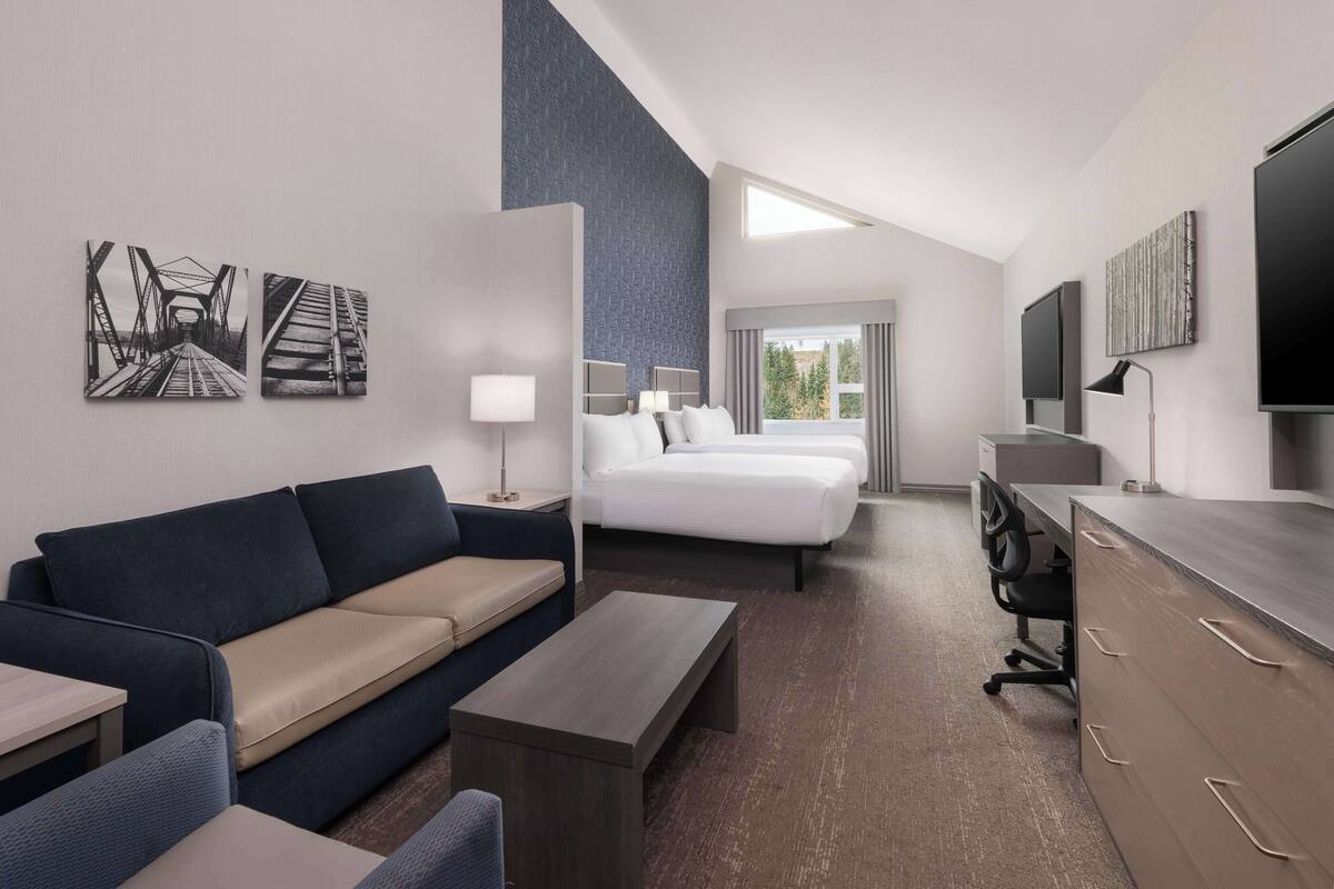 Ein Hotelzimmer mit einer Sitzecke, zwei Betten, einem Schreibtisch, einem Fernseher und Kunstwerken an den Wänden.
