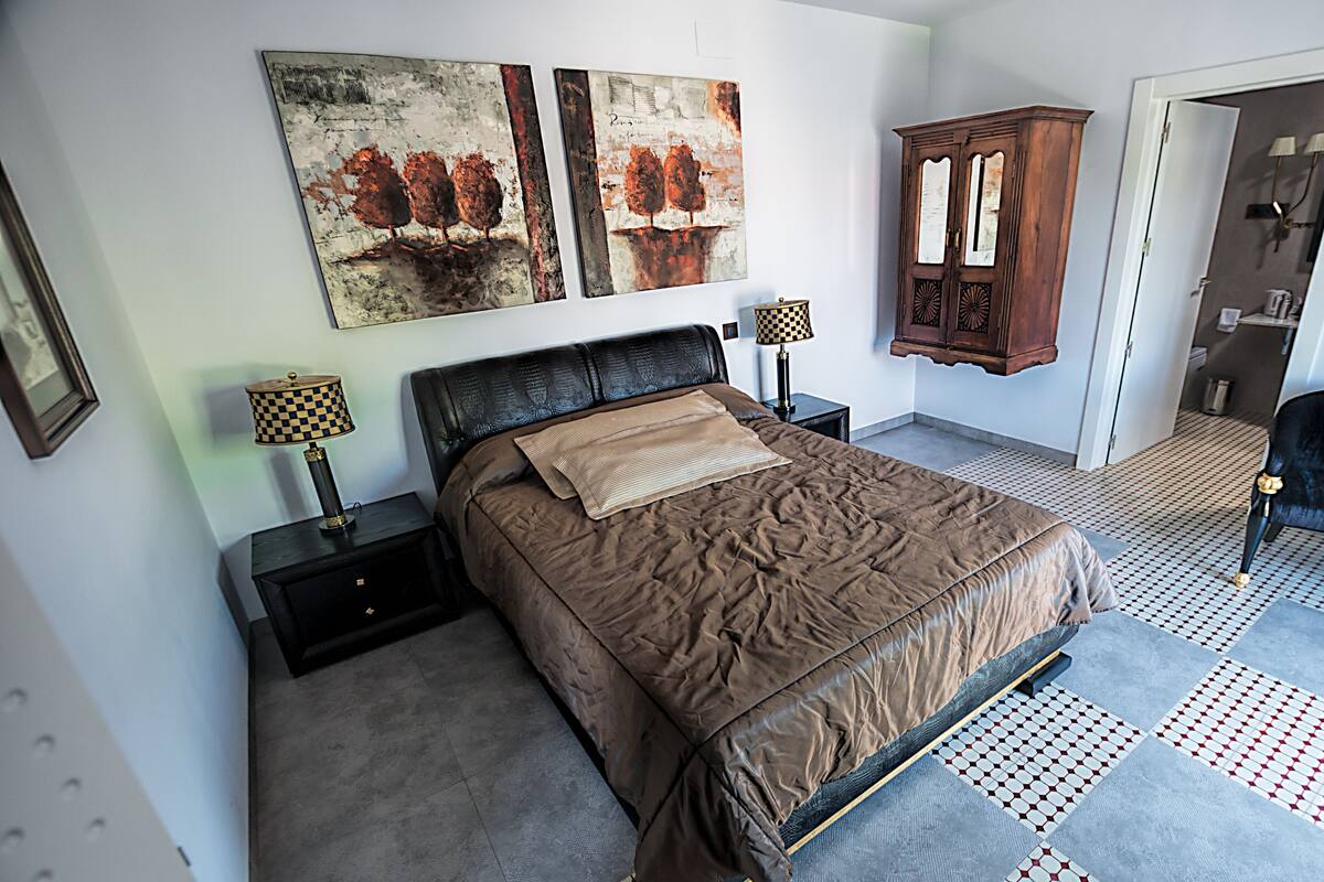 Um quarto com uma cama grande, duas mesas de cabeceira, um armário de madeira e uma obra de arte na parede.