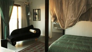 Una habitación con un sofá negro, una colcha de cama estampada en verde y un ventanal con cortinas.
