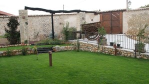 Un patio con un muro de piedra, un carro de madera y una valla metálica.