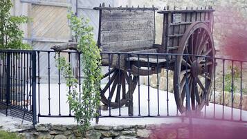 Uma antiga carruagem de madeira com rodas grandes, cercada por uma grade de metal, diante de um muro de pedra.