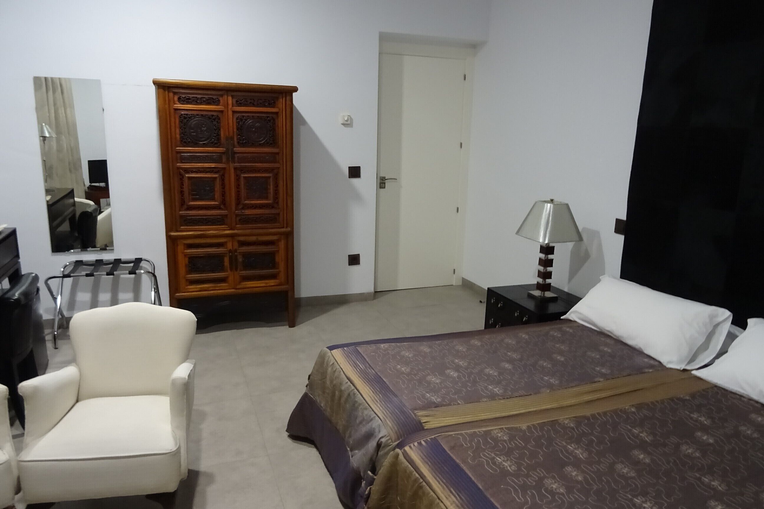 A hotel room with a bed, a chair, a wardrobe, a desk, and a lamp.