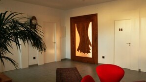 Una sala de estar moderna con un gran ventanal de madera, una silla roja, una mesita y una planta en maceta.
