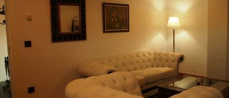 Un salón con un sofá beige grande, una mesita auxiliar, una lámpara de pie y un cuadro enmarcado en la pared.