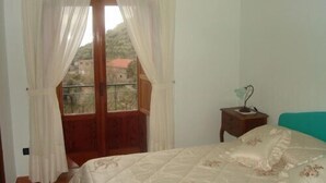 Un dormitorio con cama, mesita de noche y vistas a una colina a través de una ventana con cortinas.