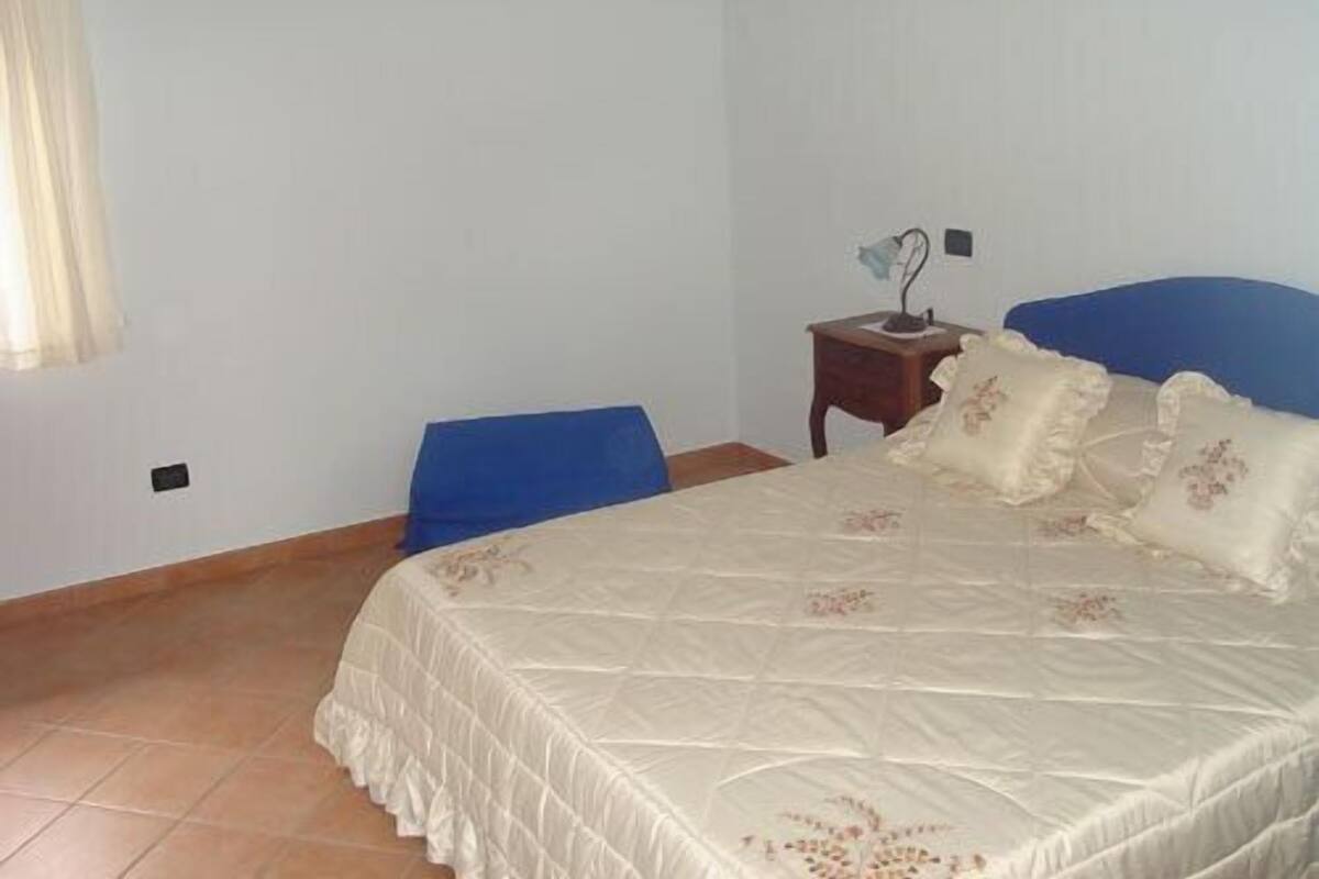 A bedroom with a bed, a nightstand, a chair, and a window with curtains.