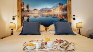 Una habitación de hotel con cama, bandeja de desayuno y un cuadro grande de un lago y montañas en la pared.