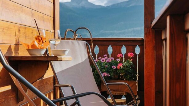 Un balcón de madera con una mesa, una silla y vistas a las montañas.