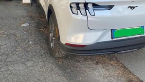 Un coche blanco estacionado en una zona cubierta para estacionamiento, con un letrero verde que señala un lugar disponible.