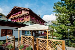 A traditional wooden building with balconies adorned with flowers, a covered outdoor seating area, and a view of mountains. - Panda  (Cortina d'Ampezzo)