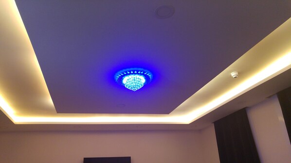 A modern ceiling with a central blue light fixture and recessed lighting along the edges.