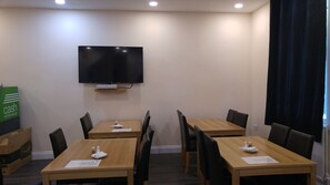 Un salón de conferencias con cuatro mesas y sillas de madera, un televisor de pantalla plana montado en la pared y un cartel que indica 'retiros de efectivo' a la izquierda.