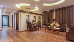 A modern living room with a wooden floor, a sofa, a coffee table, and a dining area with chairs and a table. - Rivan Palace Serviced Apartments (Riyadh)