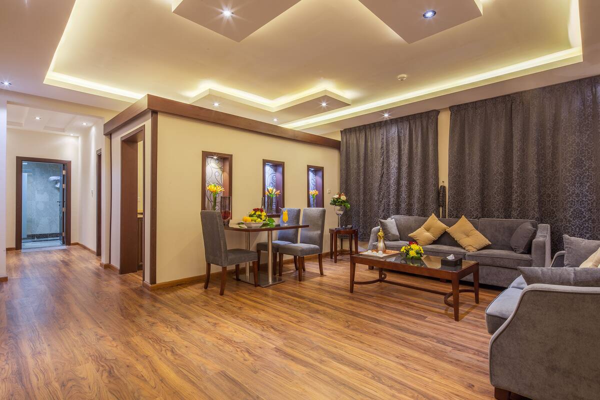 A modern living room with a wooden floor, grey sofas, a dining area with chairs, and a coffee table.