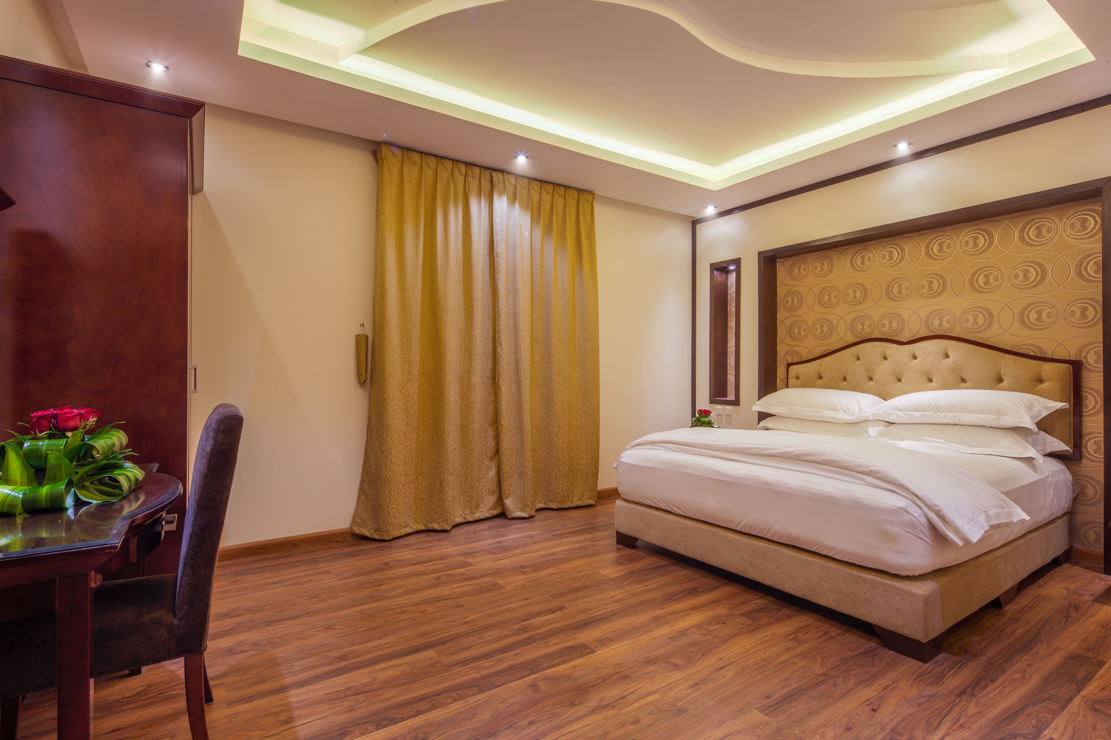 Quarto de hotel com cama, piso de madeira, mesa de jantar com cadeiras e janela com cortinas.