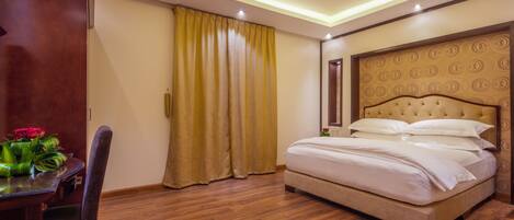 Quarto de hotel com cama, piso de madeira, mesa de jantar com cadeiras e janela com cortinas.