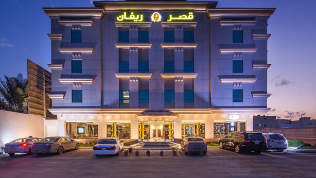 A modern hotel with a prominent entrance, multiple floors, and a parking area with several cars. - Rivan Palace Serviced Apartments (Riyadh)