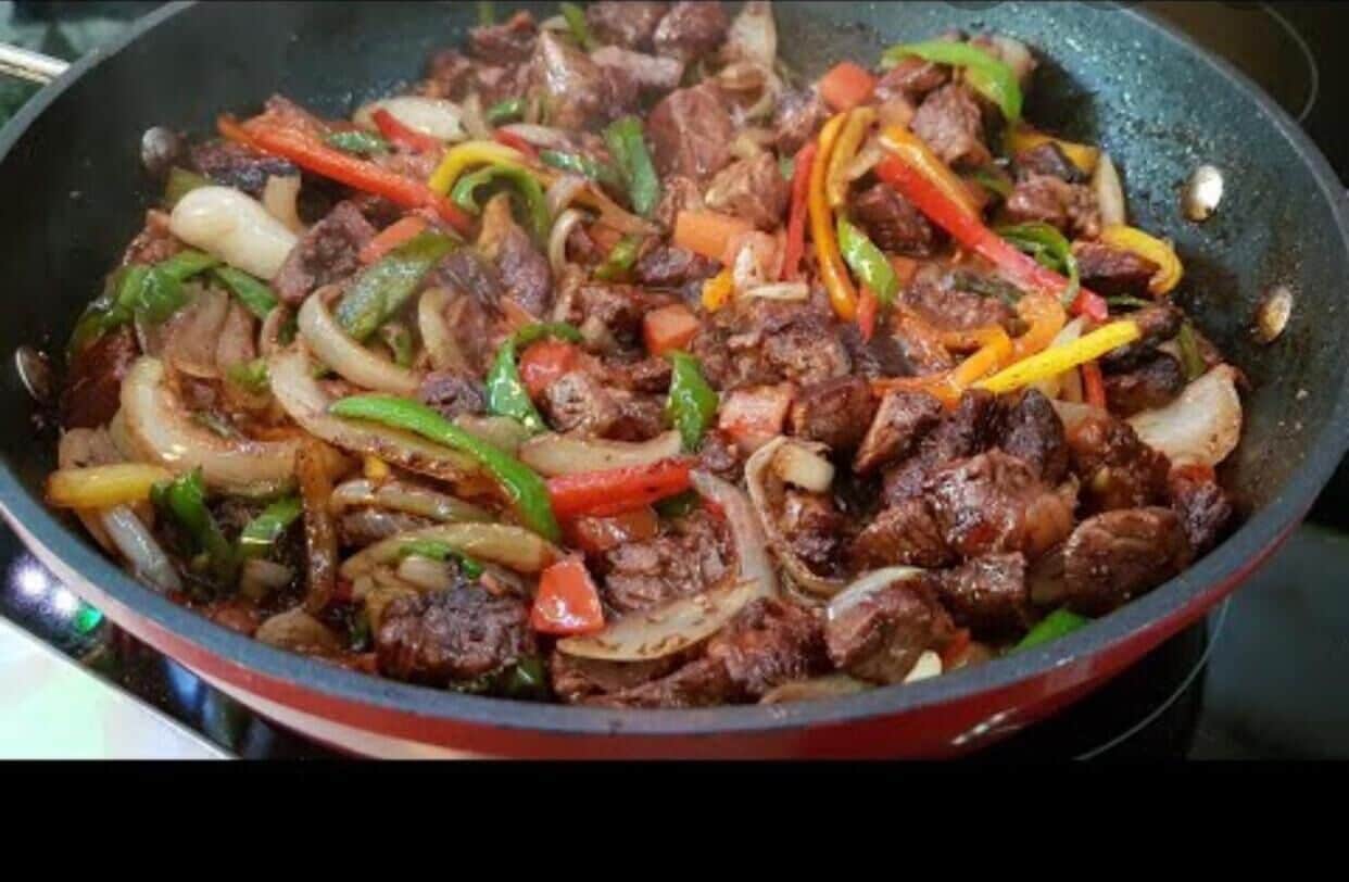 A stir-fried dish with beef, onions, and bell peppers in a pan.