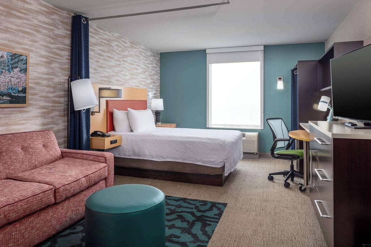 A hotel room with a bed, a desk, a chair, a sofa, and a television.