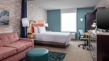 A hotel room with a bed, a desk, a chair, a sofa, and a television.