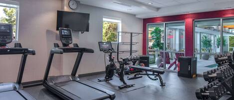 Un gimnasio con cintas de correr, una bicicleta estática, un banco para pesas y mancuernas.