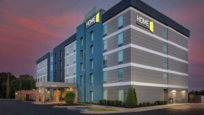 Un bâtiment d’hôtel moderne, avec une enseigne « HOME 2 », plusieurs étages et un parking.