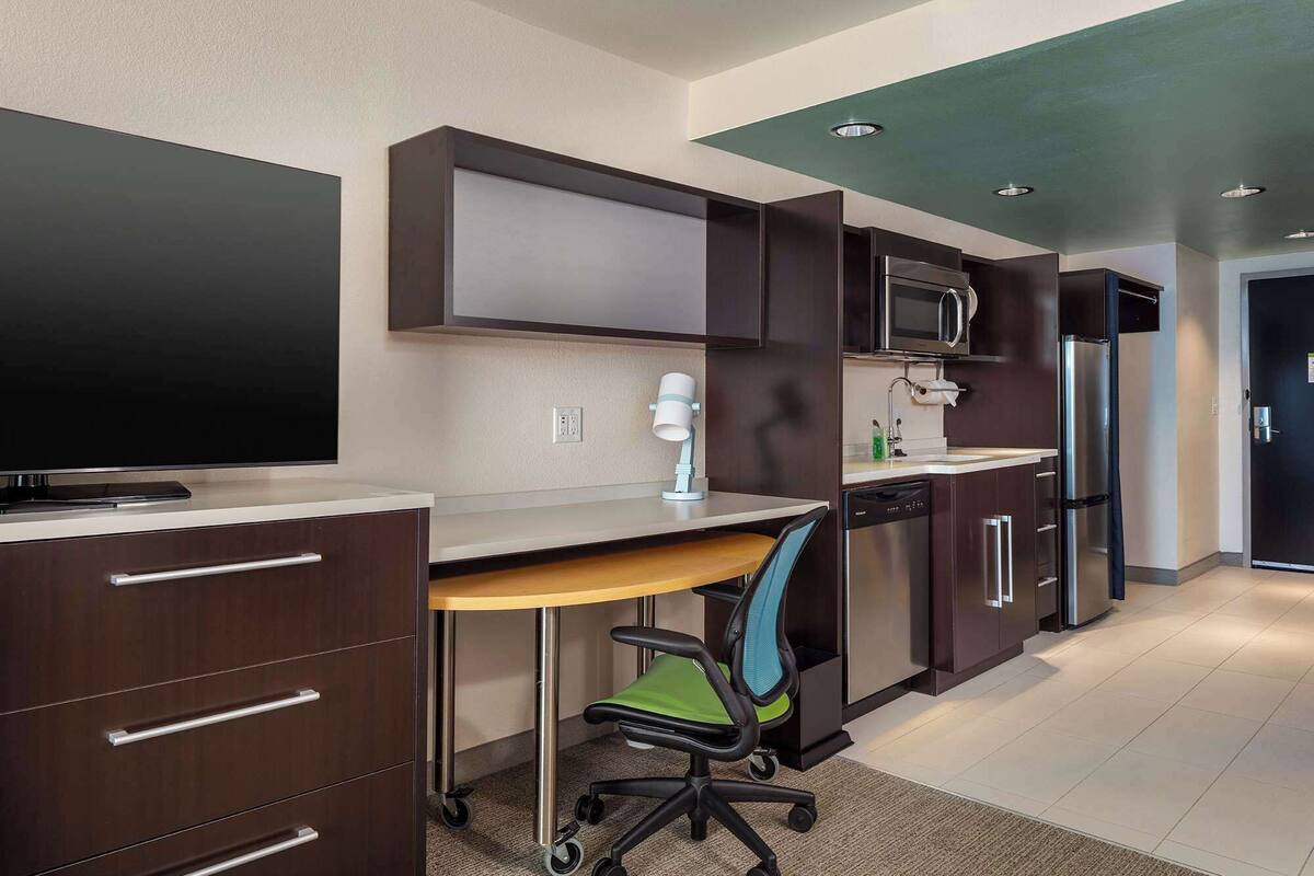A modern kitchen with dark cabinets, a microwave, a refrigerator, and a desk with a chair.