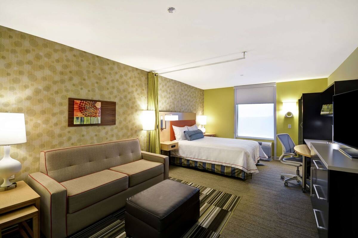 A hotel room with a bed, a sofa, a desk, a TV, and a window.