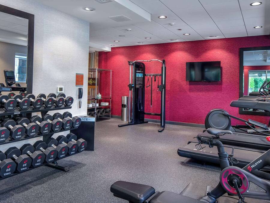 Un gimnasio con equipo de levantamiento de pesas, cintas de correr y una pared de ladrillo rojo.