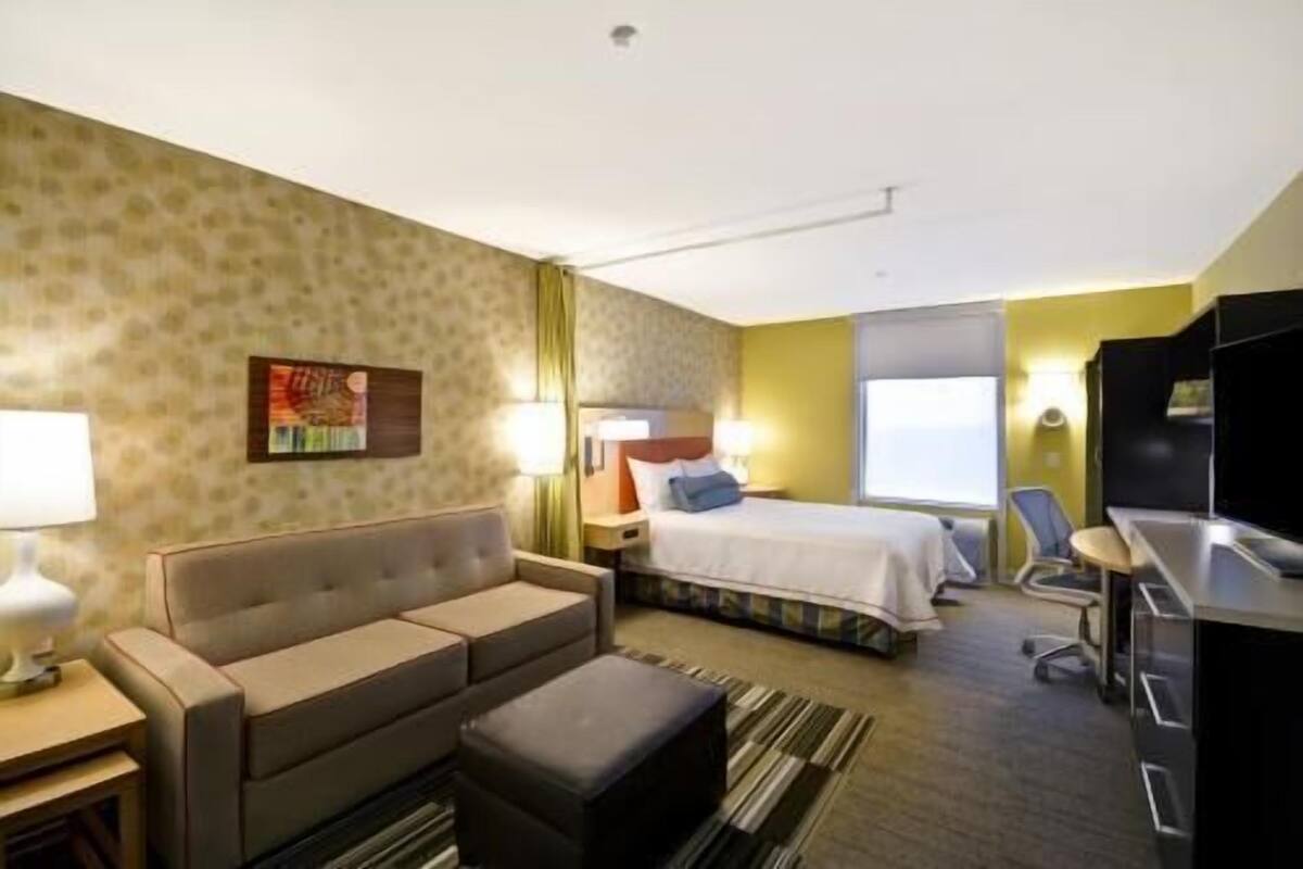 A hotel room with a bed, a sofa, a desk, and a TV.