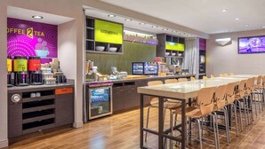 Un café moderne avec un long comptoir, des machines à café, un réfrigérateur et un écran de télévision.