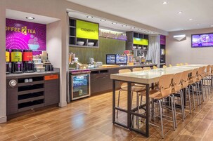 Un café moderno con una barra alargada, máquinas de café, un refrigerador y una pantalla de televisión.