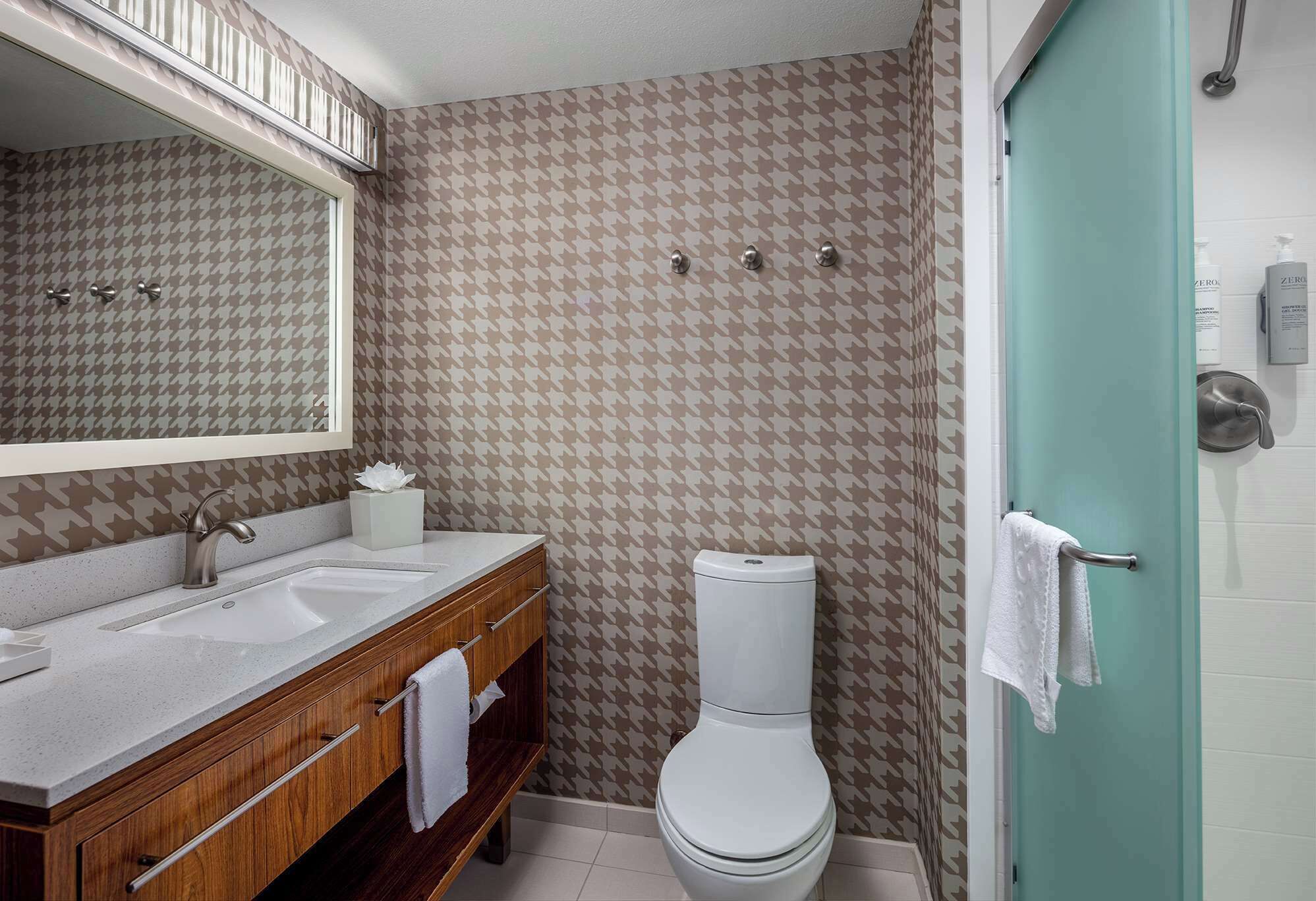 A bathroom with a houndstooth patterned wall, a white toilet, a sink with a wooden vanity, and a mirror above the vanity.