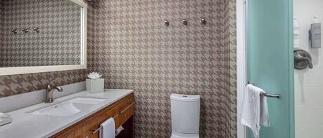 A bathroom with a houndstooth patterned wall, a white toilet, a sink with a wooden vanity, and a mirror above the vanity.