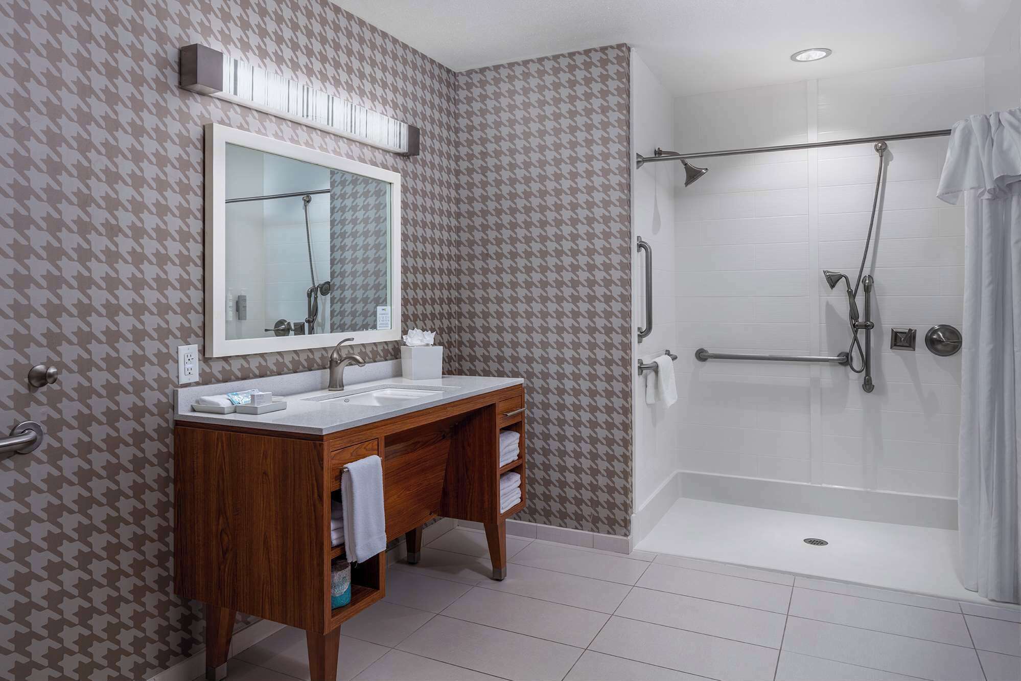 A modern bathroom with a vanity, mirror, shower, and a houndstooth patterned wall.