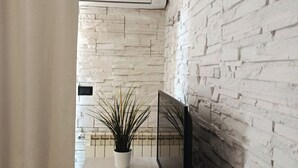 A modern room with a white brick wall, a desk with a computer monitor, a plant, and a window with curtains. - Central Park B&B (Casarile)