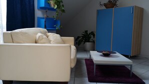 A living room with a beige sofa, a white coffee table, a blue cabinet, and a potted plant. - Central Park B&B (Casarile)
