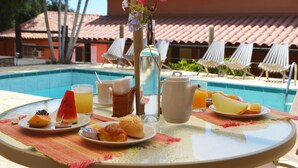 Una tavola imbandita per la colazione, con un piatto di frutta, un teiera, un bicchiere di succo d'arancia e un cesto di vimini.