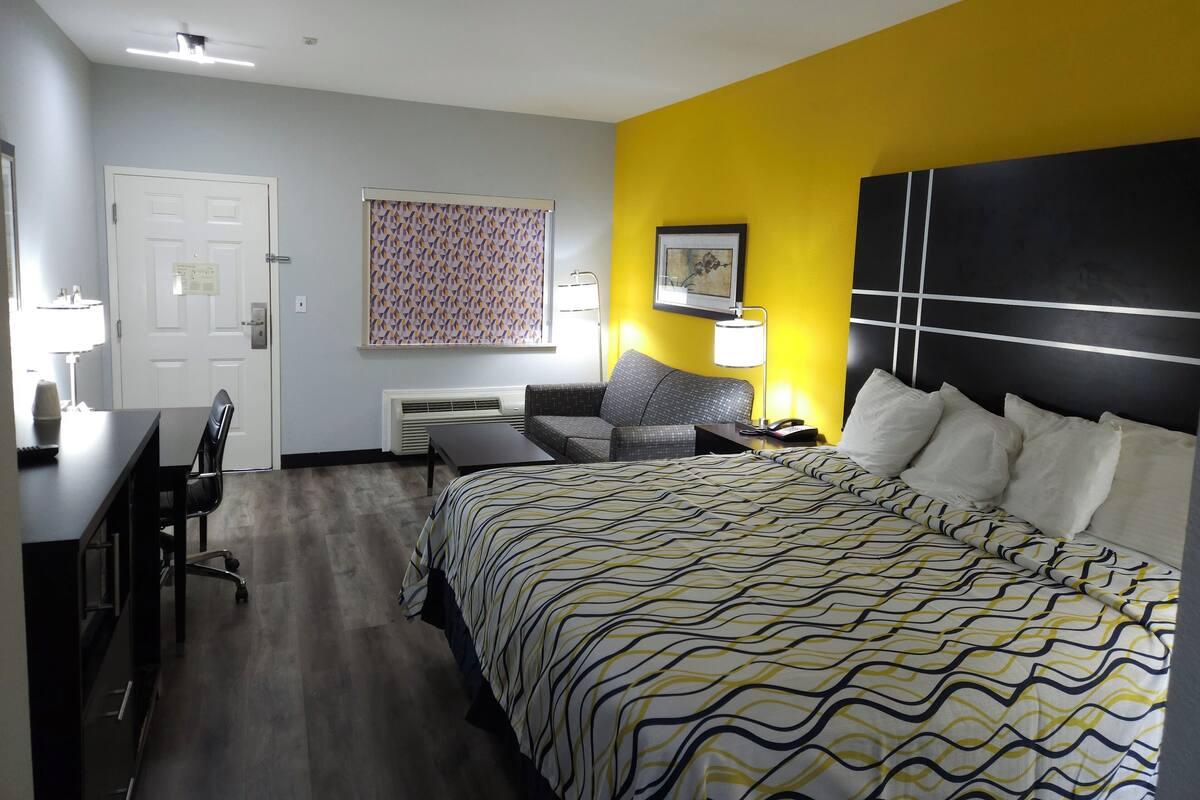 Een hotelkamer met een bed, een bureau met stoel, een bank en een nachtkastje met lamp.