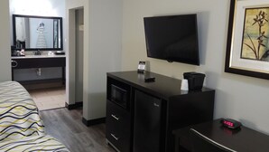 Ein Hotelzimmer mit Bett, Schreibtisch, Stuhl, Fernseher, Mikrowelle und kleinem Kühlschrank.
