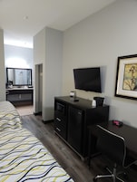 Una habitación de hotel con cama, escritorio, silla, televisión, microondas y un refrigerador pequeño.