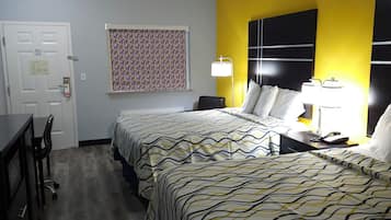 A hotel room with a bed, bedside table, lamp, and a desk with a chair.