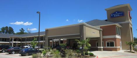 A hotel with a covered parking area, multiple cars parked, and a clear blue sky.