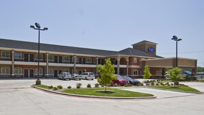 A hotel with a parking lot, multiple cars, and a clear sky.