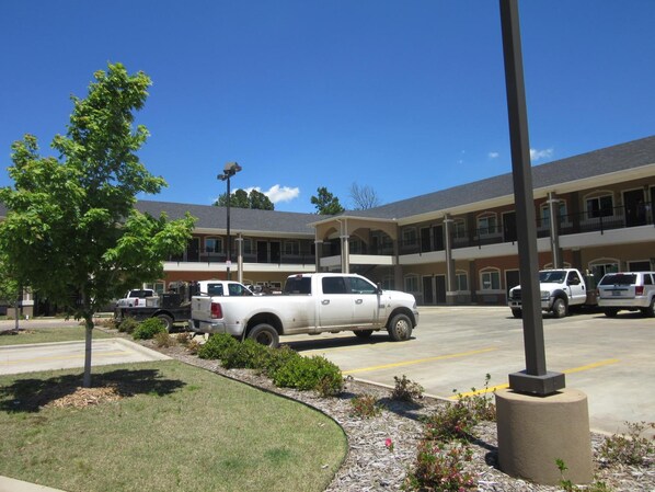 A multi-story hotel with a parking lot. There are several white pickup trucks parked in the lot. The hotel has a flat roof and a balcony on the second floor.