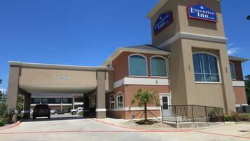 An Executive Inn & Suites building with a clear driveway, a covered parking area, and a small landscaped area with a palm tree.